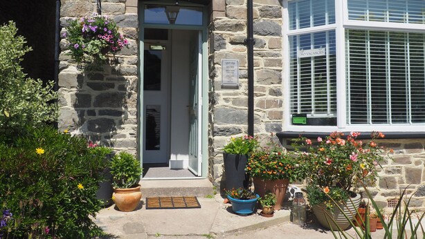 A stone building with a door, a window with shutters, and various potted plants. - South View Guest House (Lynton)