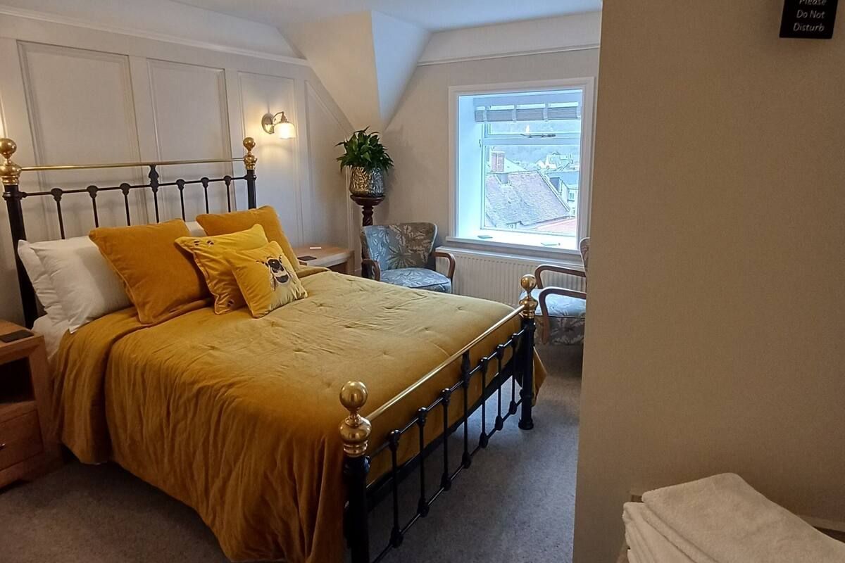 Ein Schlafzimmer mit Bett, Nachttischen, einem Sessel, einem Fenster und einem hängenden Schild.