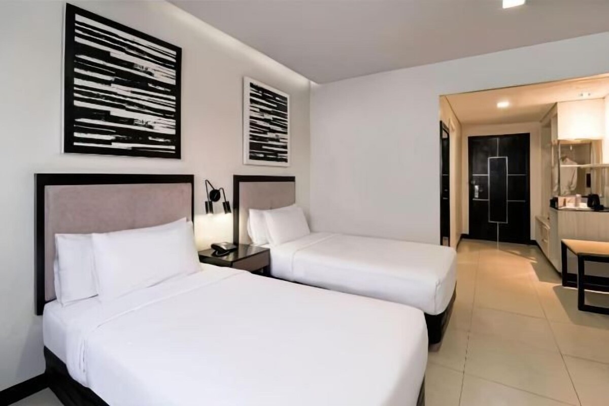 A hotel room with two beds, a desk, a chair, and a kitchenette.