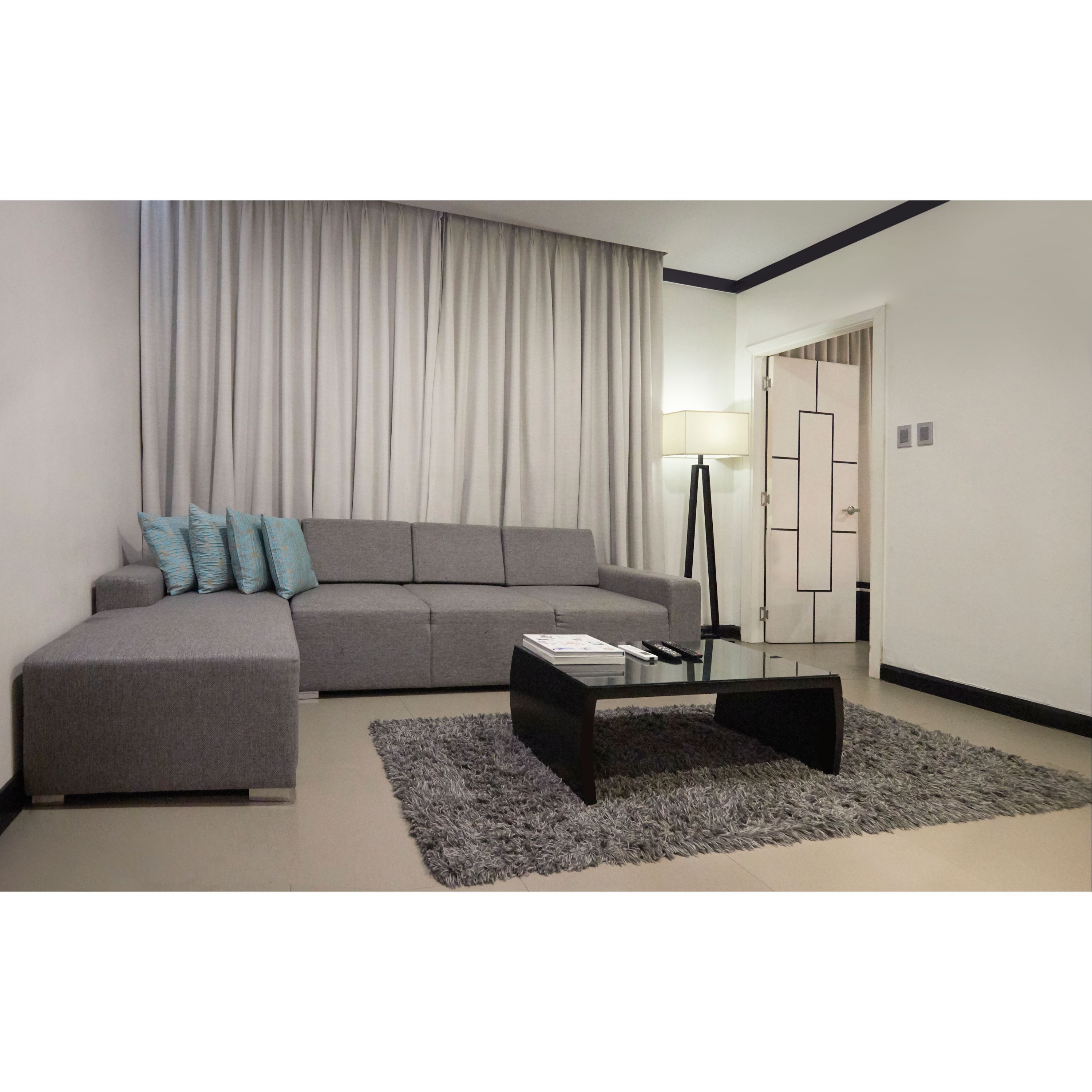 A modern living room with a grey sectional sofa, a glass coffee table, and a grey shag rug.