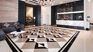 A modern lobby with a geometric patterned floor, a sofa with decorative pillows, a coffee table, a chandelier, and a reception desk with a decorative wall. - Summit Hotel Magnolia (Quezon City)