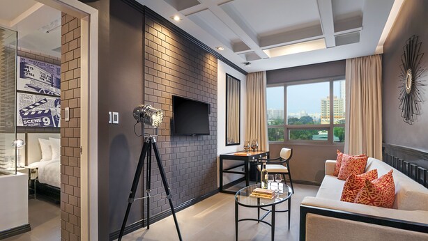 A modern living room with a brick accent wall, a mounted TV, a tripod, a glass coffee table, and a sofa with patterned cushions. - Summit Hotel Magnolia (Quezon City)