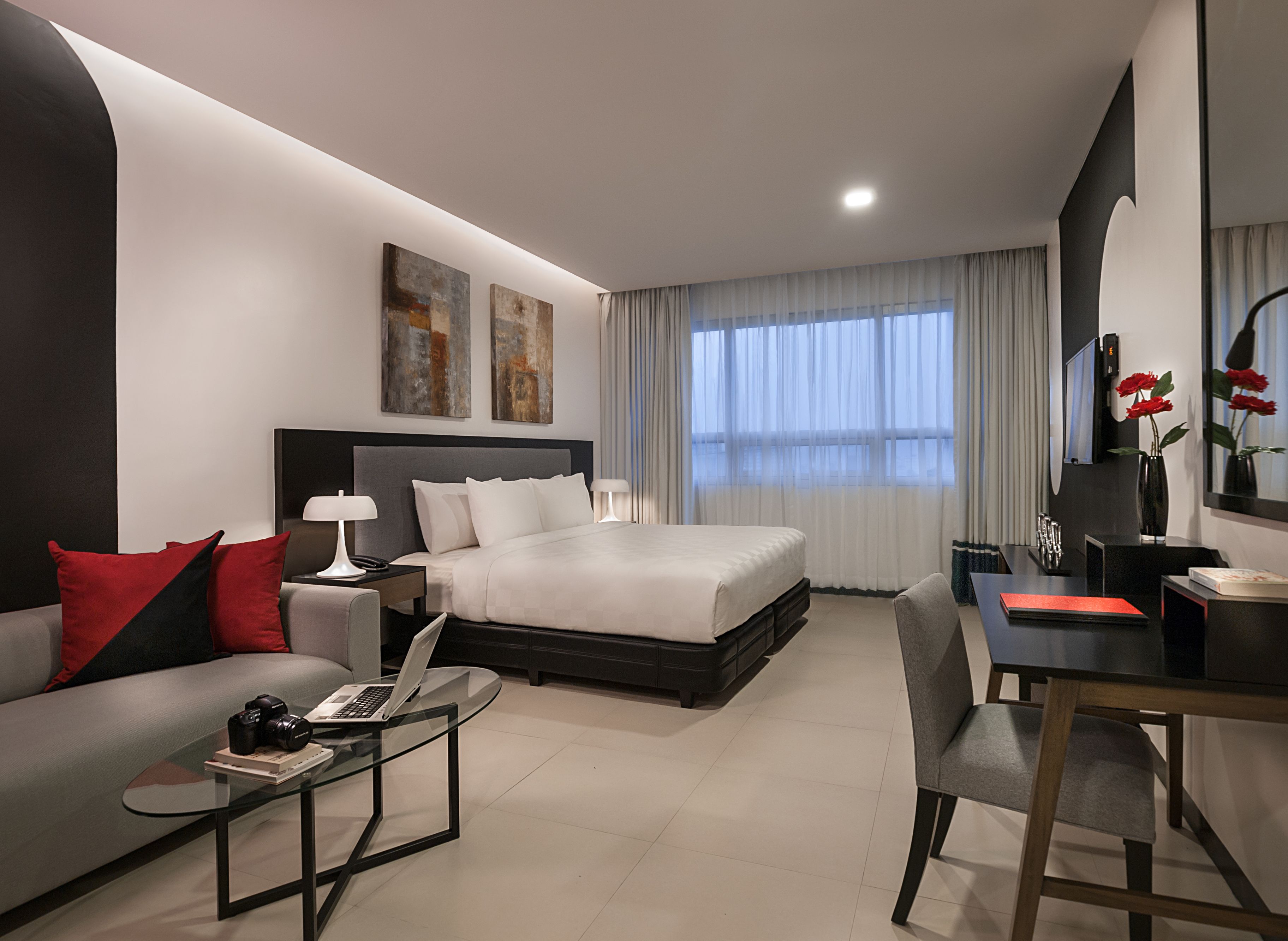 A modern hotel room with a large bed, a desk, a sofa, and a glass coffee table.