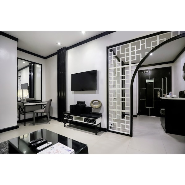 A modern living room with a flat-screen TV, a dining area with a table and chairs, and a kitchen area with a counter and cabinets.
