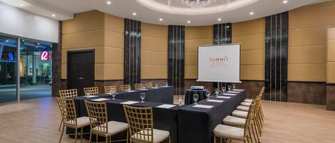 A conference room with a long table, chairs, a projector screen, and a chandelier.