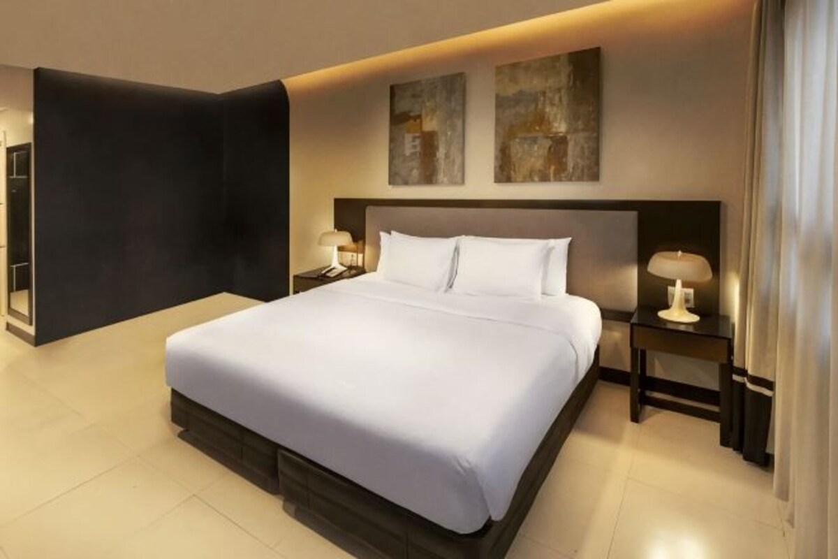 A modern hotel room with a large bed, two bedside tables with lamps, and abstract artwork on the wall.