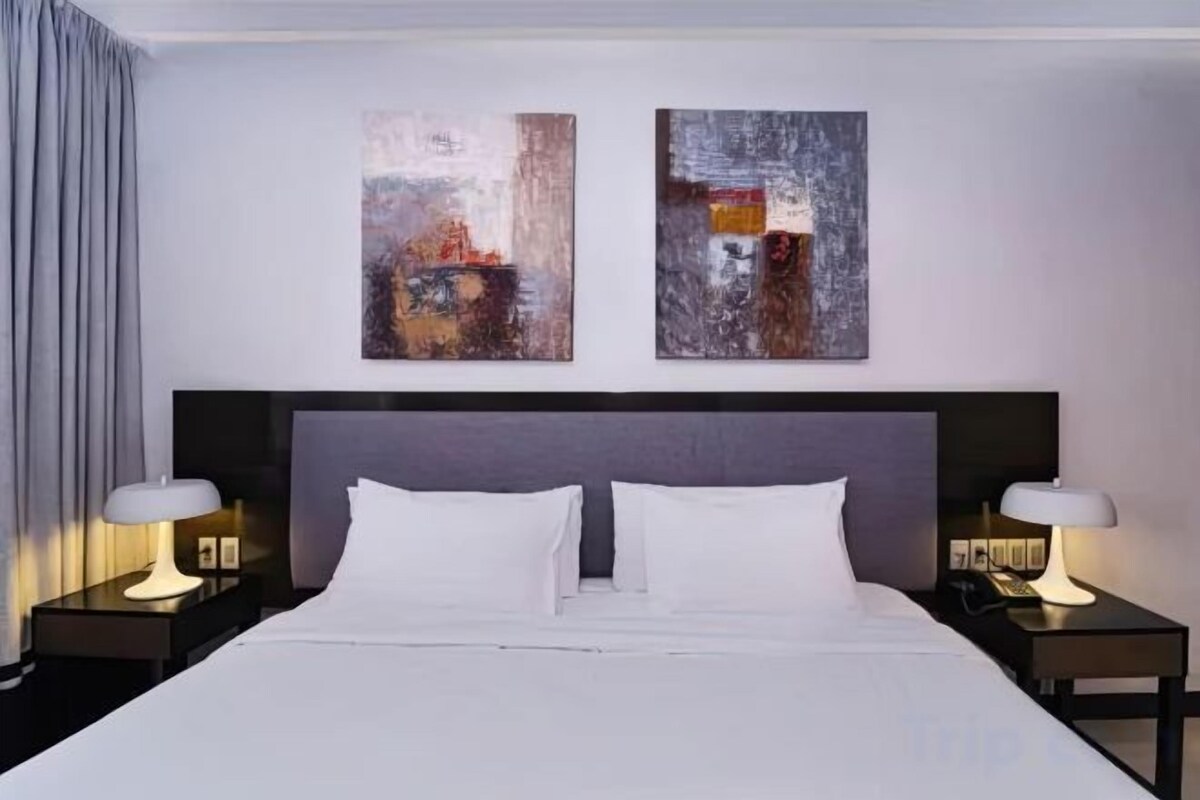 Een hotelkamer met een groot bed, twee nachtkastjes en abstracte wanddecoratie.