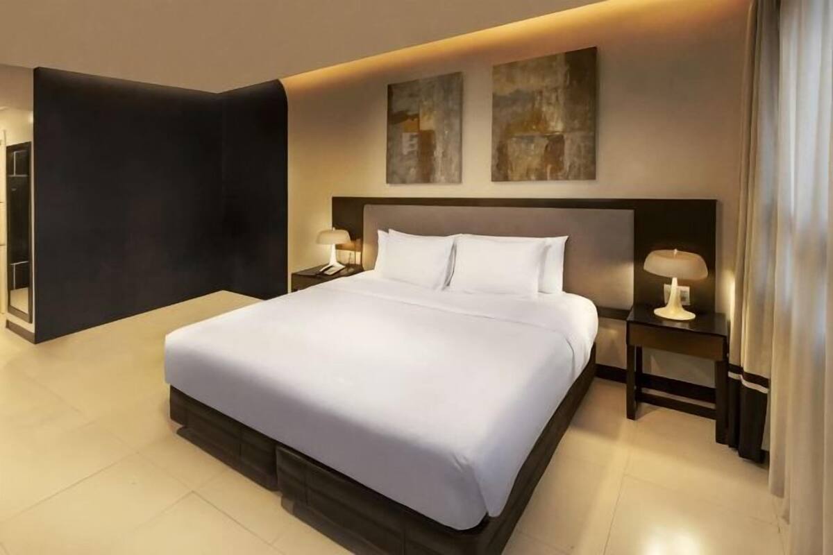 A modern hotel room with a large bed, two bedside tables with lamps, and abstract artwork on the wall.