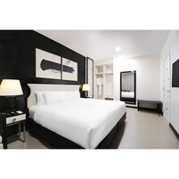 Una habitación de hotel moderna con una cama grande, mesitas de noche con lámparas, un vestidor y un baño con ducha e inodoro.