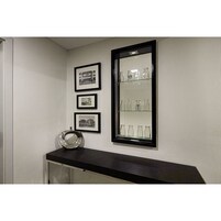 A wall with three framed black and white photographs and a glass display case with empty bottles.