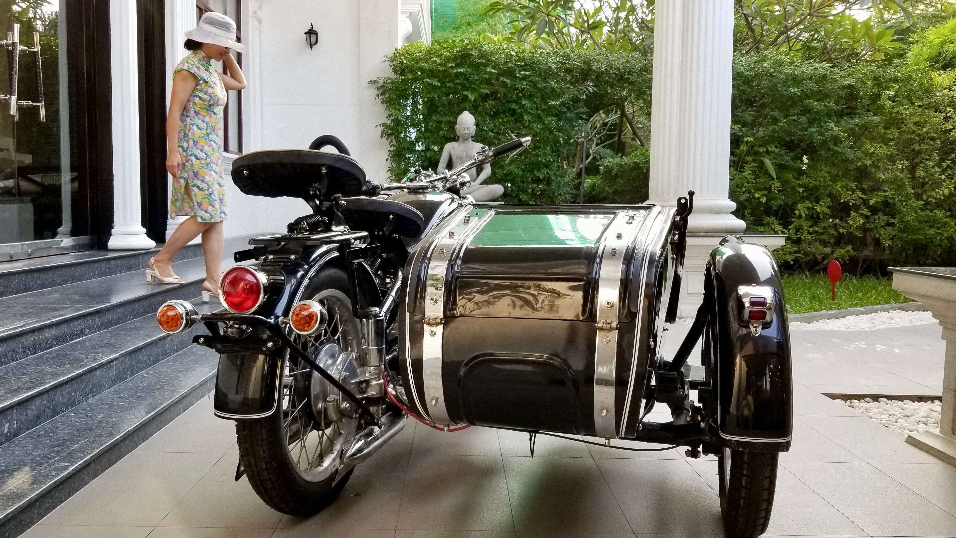 Una motocicleta clásica con sidecar estacionada frente a un edificio con columnas blancas y una estatua.