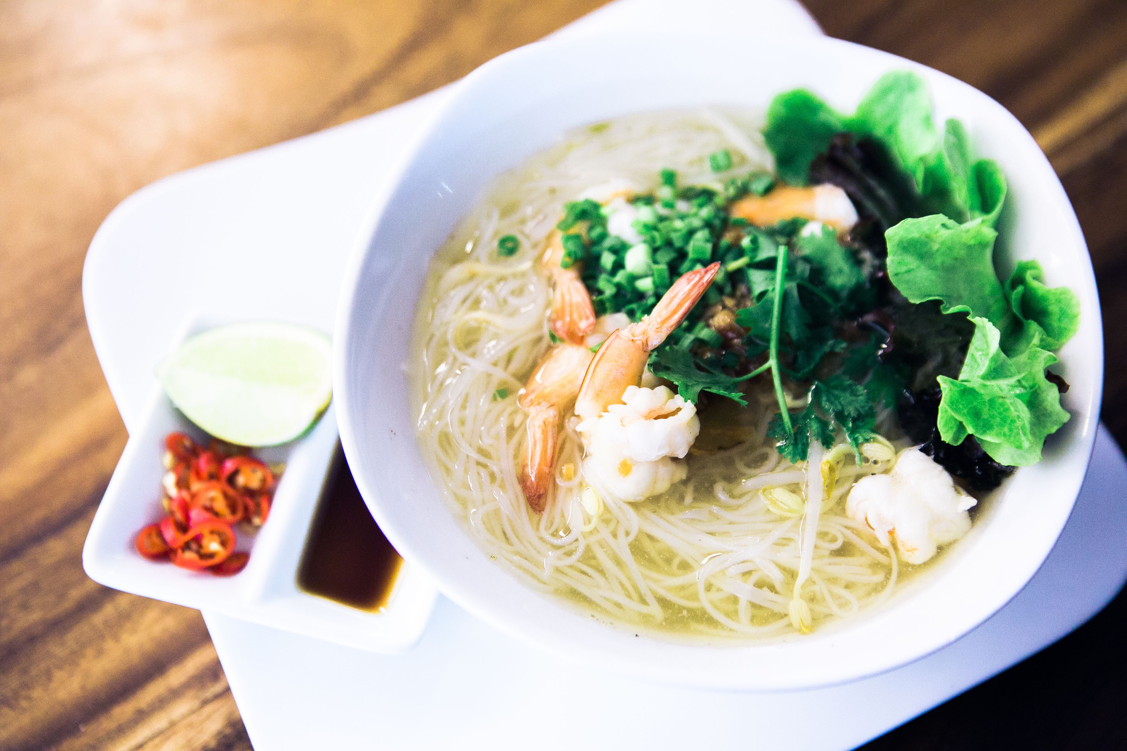 A bowl of noodle soup with shrimp, greens, and a side of lime and chili.