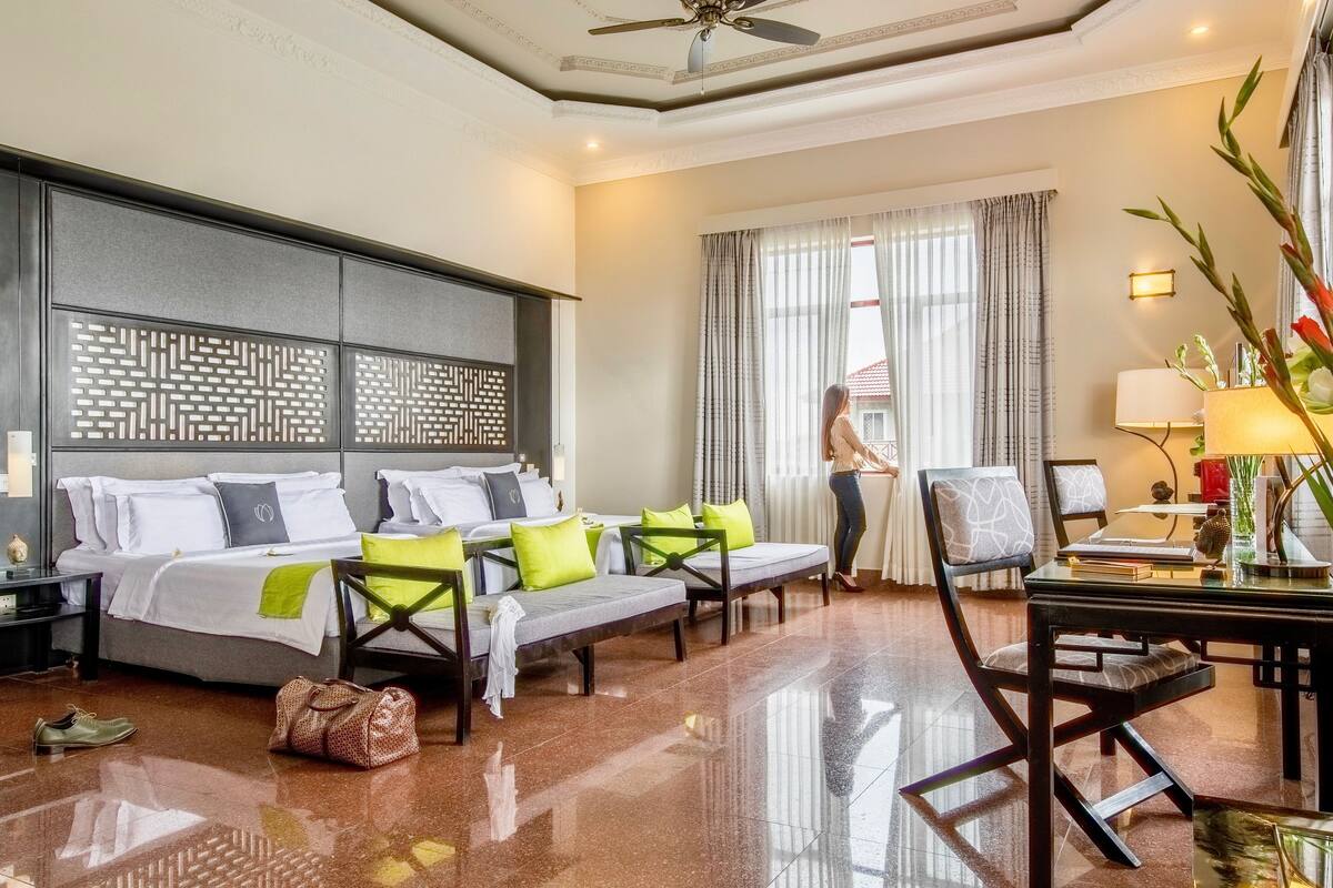 A hotel room with a bed, a desk, a chair, a window with curtains, and a decorative wall panel.
