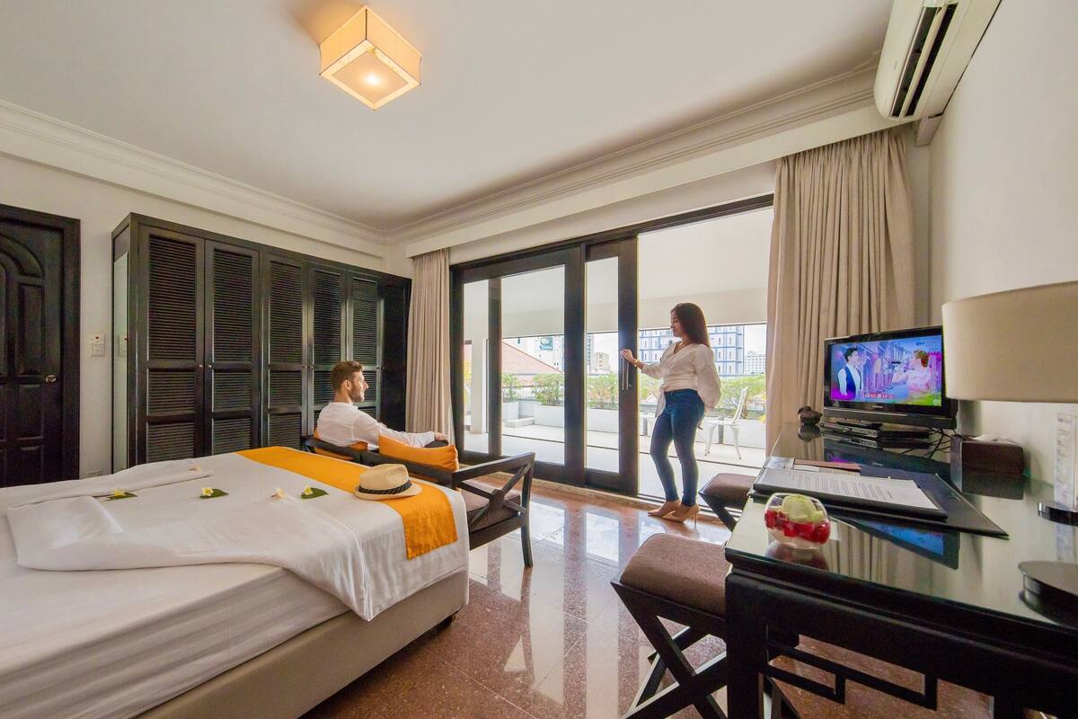 A hotel room with a bed, a desk with a computer, a television, and a view of the outside.