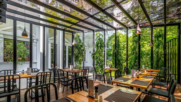 Ein Restaurant mit großen Fenstern, Holztischen und schwarzen Stühlen.