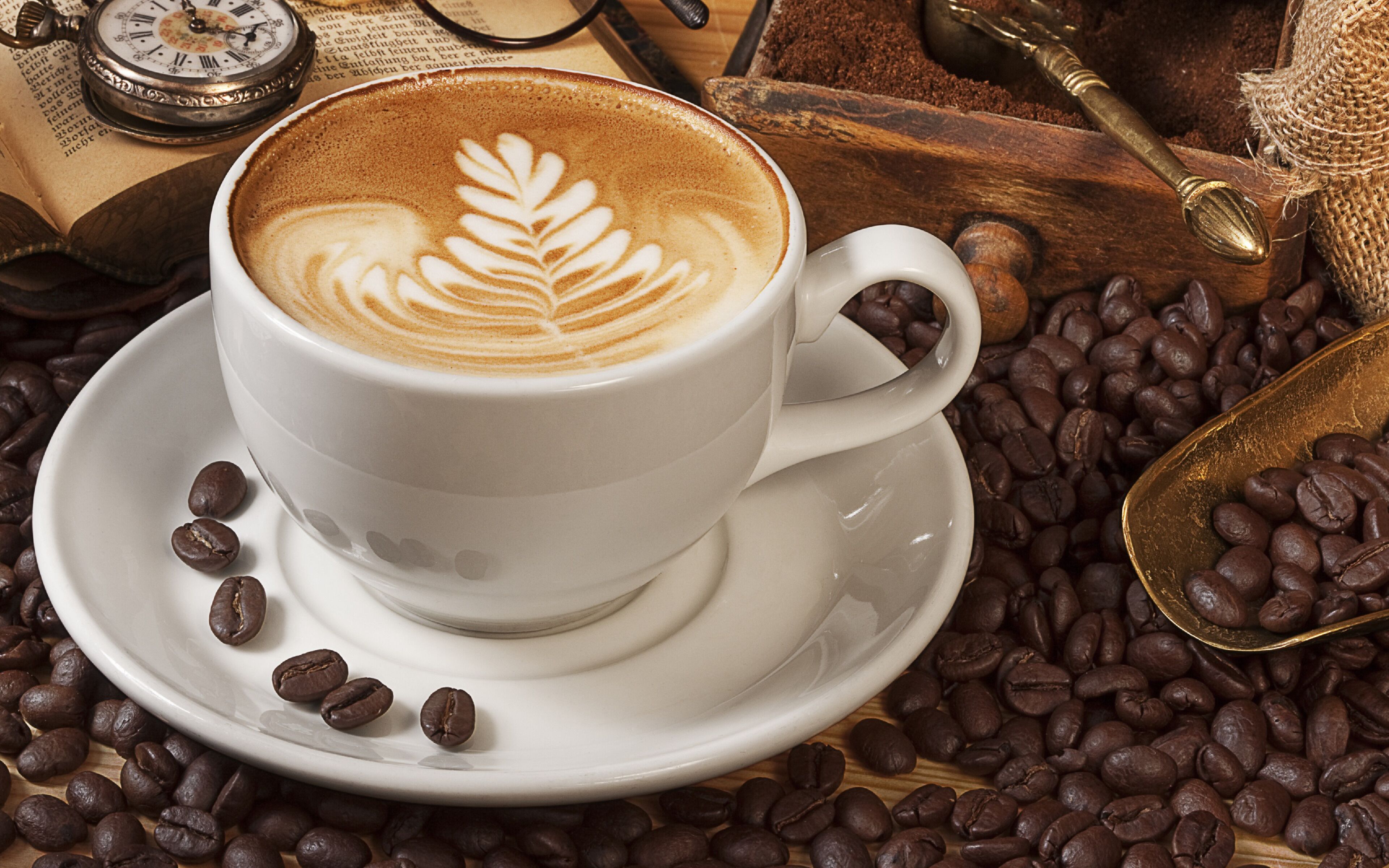 A cup of coffee with latte art on a saucer surrounded by coffee beans.