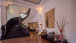 Eine prachtvolle Treppe mit geschwungener Form, eine Statue und ein Bücherregal in einem hell erleuchteten Eingangsbereich.