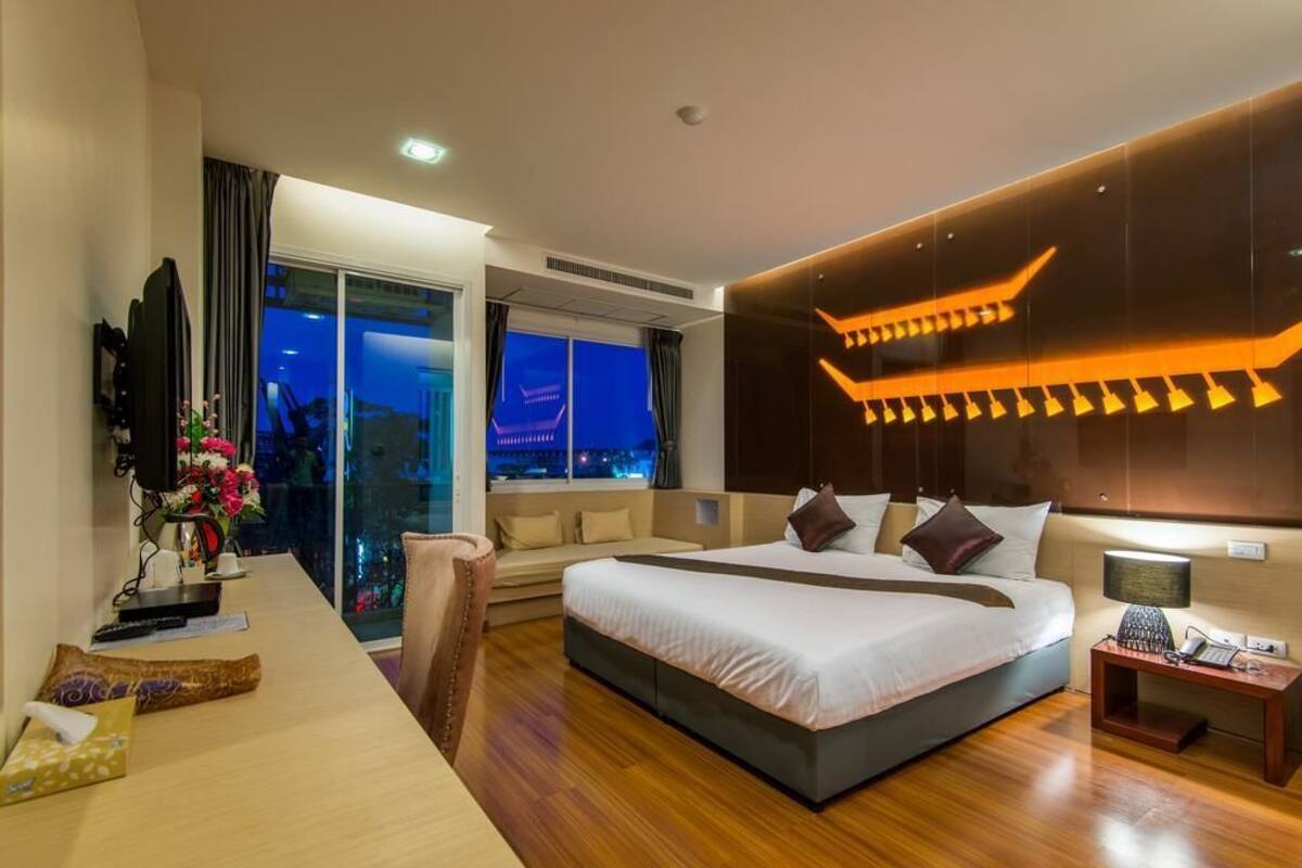 Quarto de hotel moderno com uma cama grande, uma mesa com computador, uma cadeira e vista para a cidade à noite.