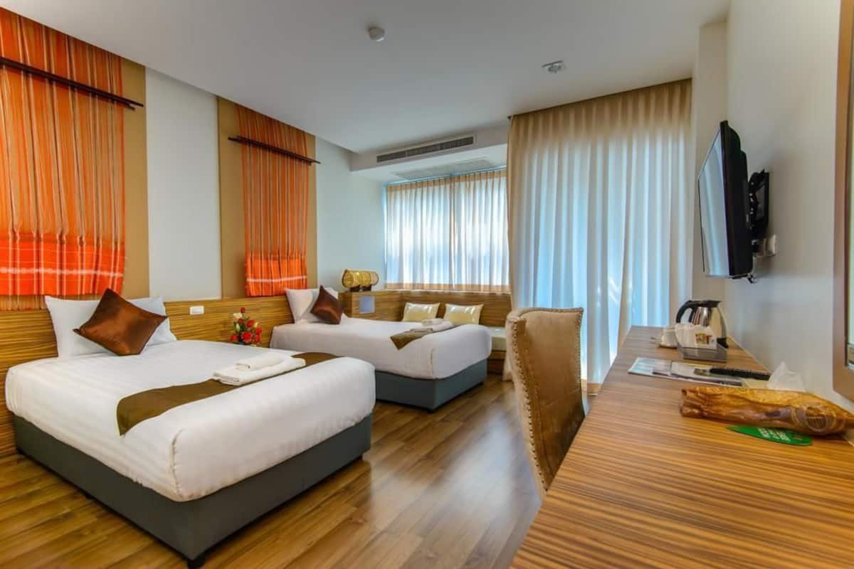 Quarto de hotel com duas camas, uma mesa de trabalho com televisão e uma janela com cortinas.