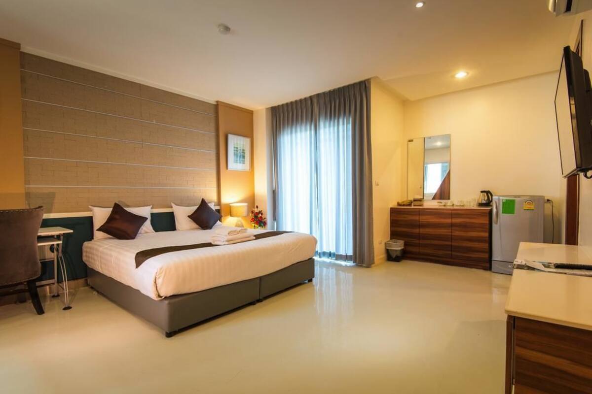 Quarto de hotel com cama grande, escrivaninha, cadeira, cômoda, espelho e televisão.