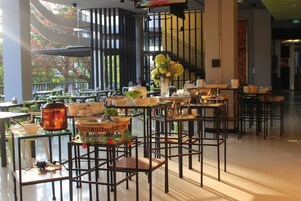 Un comedor moderno con varias mesas y sillas, un ventanal con vistas a árboles, y una escalera al fondo.