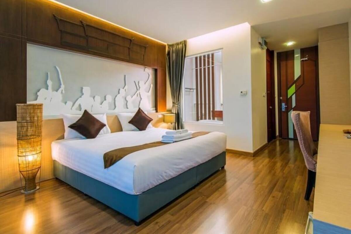 Quarto de hotel moderno com uma cama grande, luminária de cabeceira, um objeto decorativo na parede e piso de madeira.