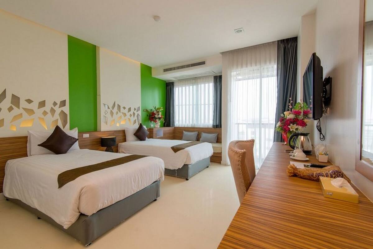 Quarto de hotel com duas camas, uma escrivaninha de madeira, televisão e uma janela grande com cortinas.