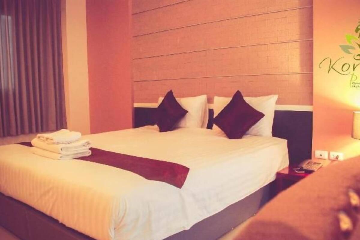 Cama bem arrumada com almofadas e toalha dobrada, cabeceira de madeira e parede com um logotipo.
