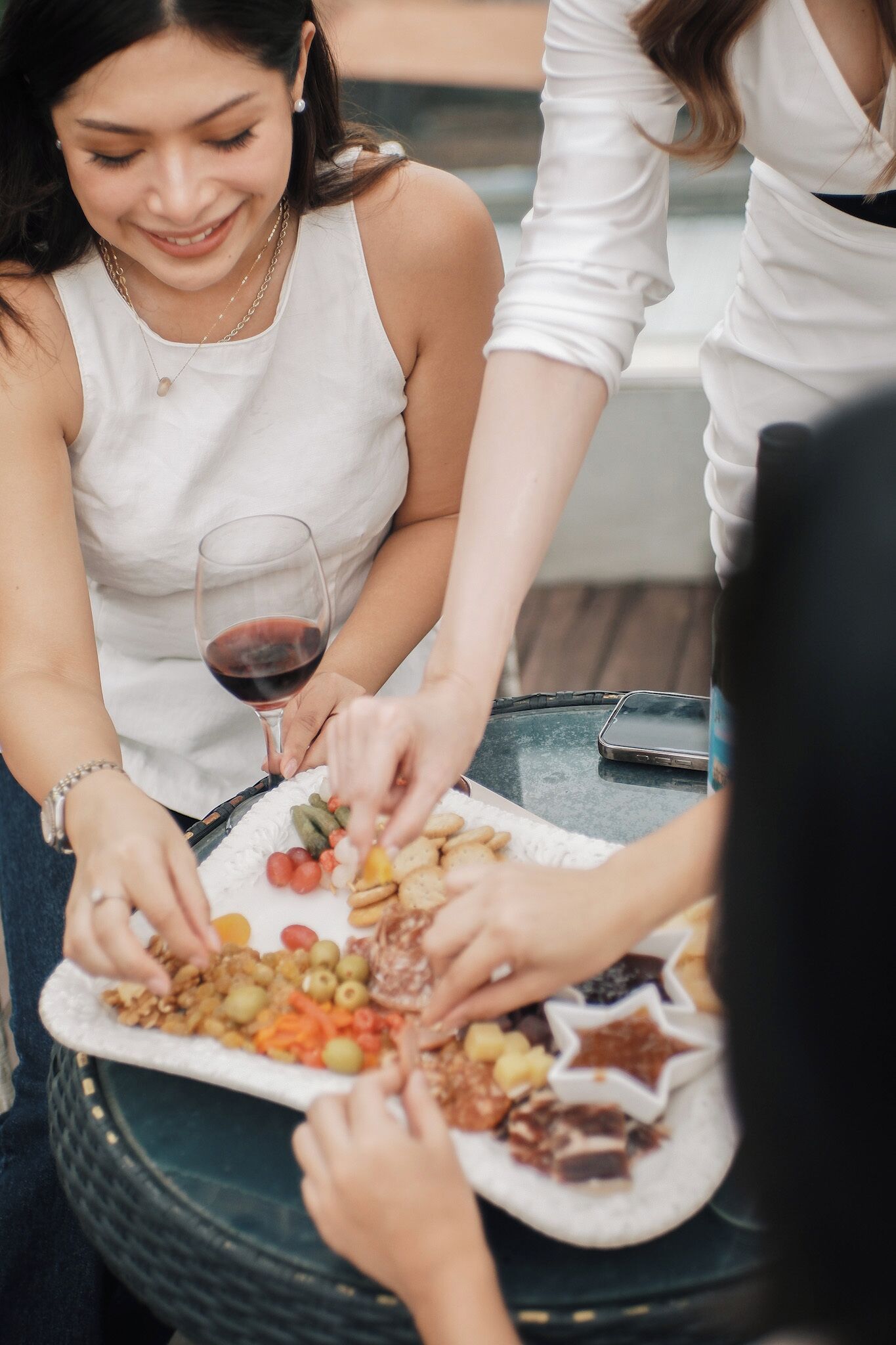 A group of people sitting around a table with a variety of snacks and a glass of red wine.