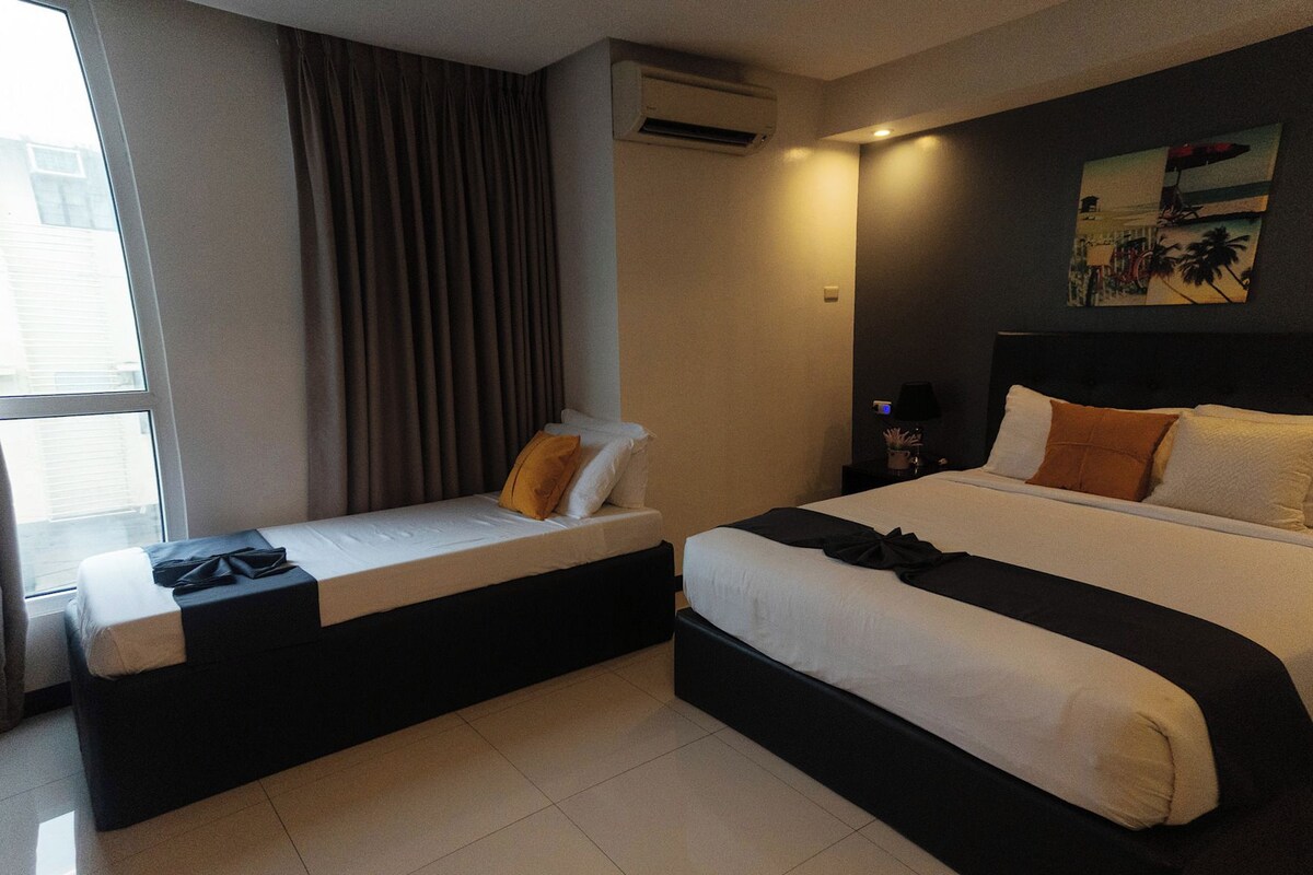 Une chambre d’hôtel avec deux lits, une fenêtre avec des rideaux, un appareil de climatisation, une table de chevet avec une lampe et un tableau au mur.