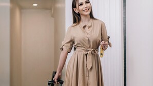 A person in a beige dress with a suitcase, standing in a hallway with a white door and a light switch on the wall. - The Upperhouse Hotel – Boutique Stay with City & River Views (Cagayan de Oro)