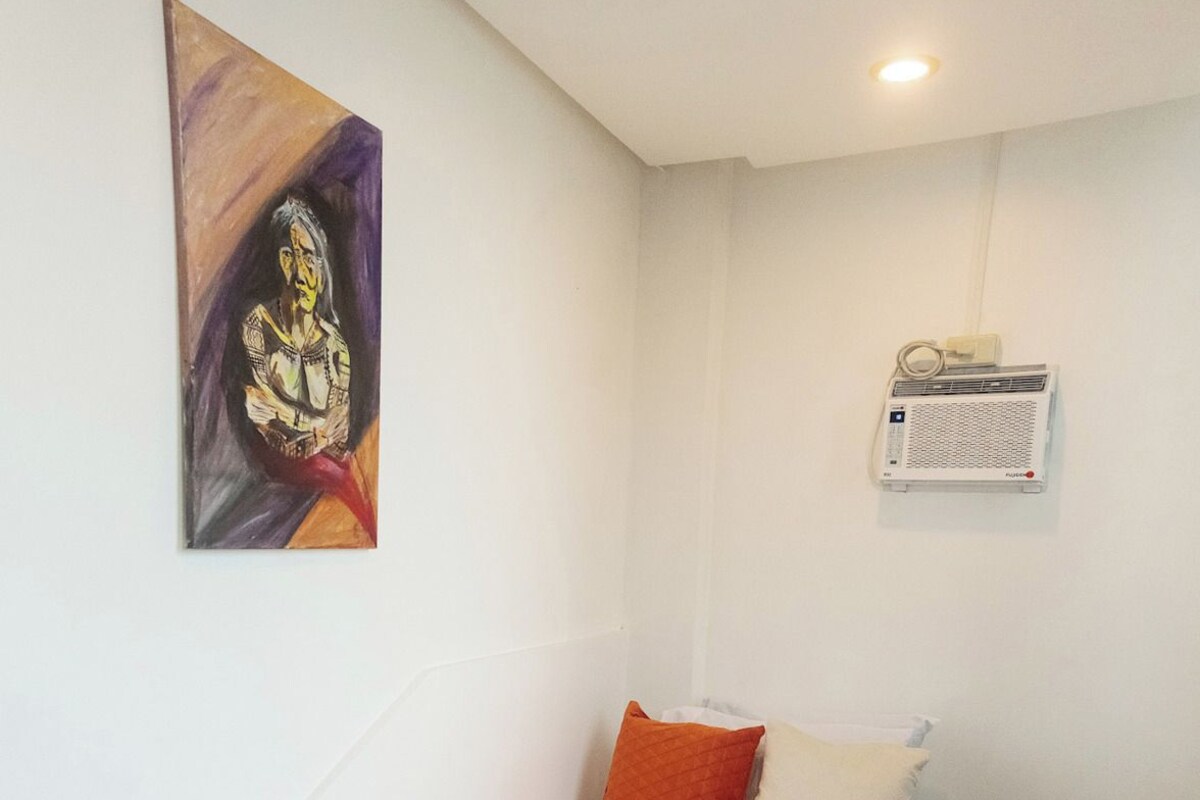 Une chambre à coucher avec un lit, des oreillers, une couverture, un climatiseur fixé au mur et un tableau.