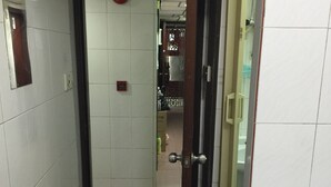 A narrow hallway with white tiled walls, a door leading to a room with a bed, and a red circular object on the wall. - China Guest Hostel (Kowloon)