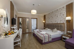 A hotel room with two beds, a desk with a fruit bowl, a mirror, and a television. - Kustur Club Holiday Village (Kusadasi)
