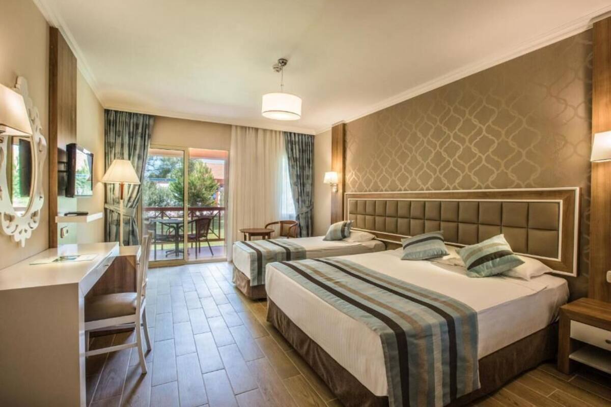 Una camera d'albergo con due letti, una scrivania, una sedia, un televisore e un balcone con tavolo e sedie.