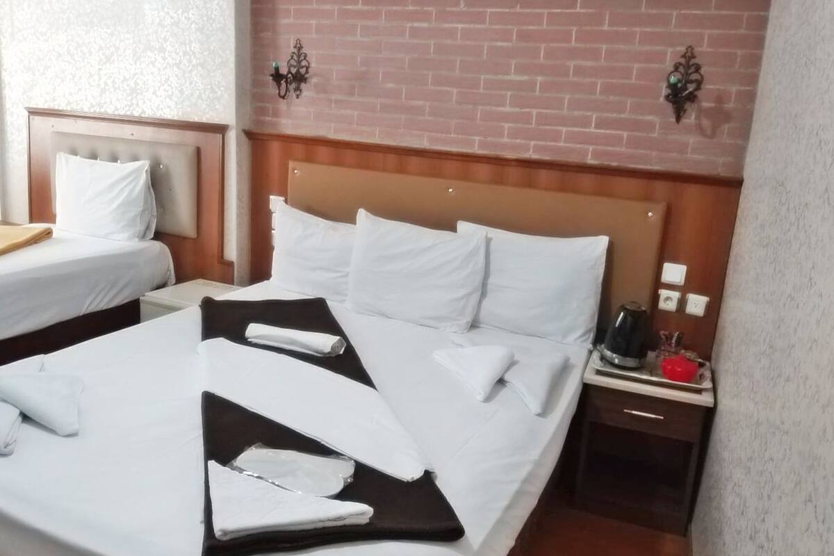 A hotel room with a large bed, two smaller beds, a nightstand with a coffee maker, and a brick wall.