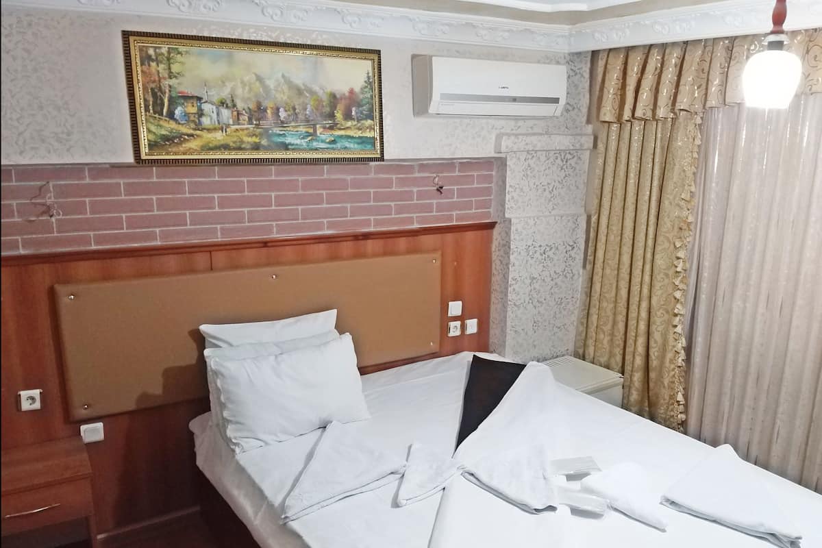 A hotel room with a wooden headboard, a painting above the bed, an air conditioning unit, and a curtain.