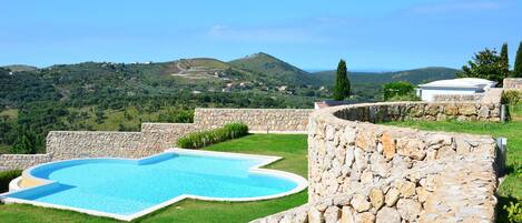 Una piscina con un muro de piedra y vistas a un paisaje montañoso.