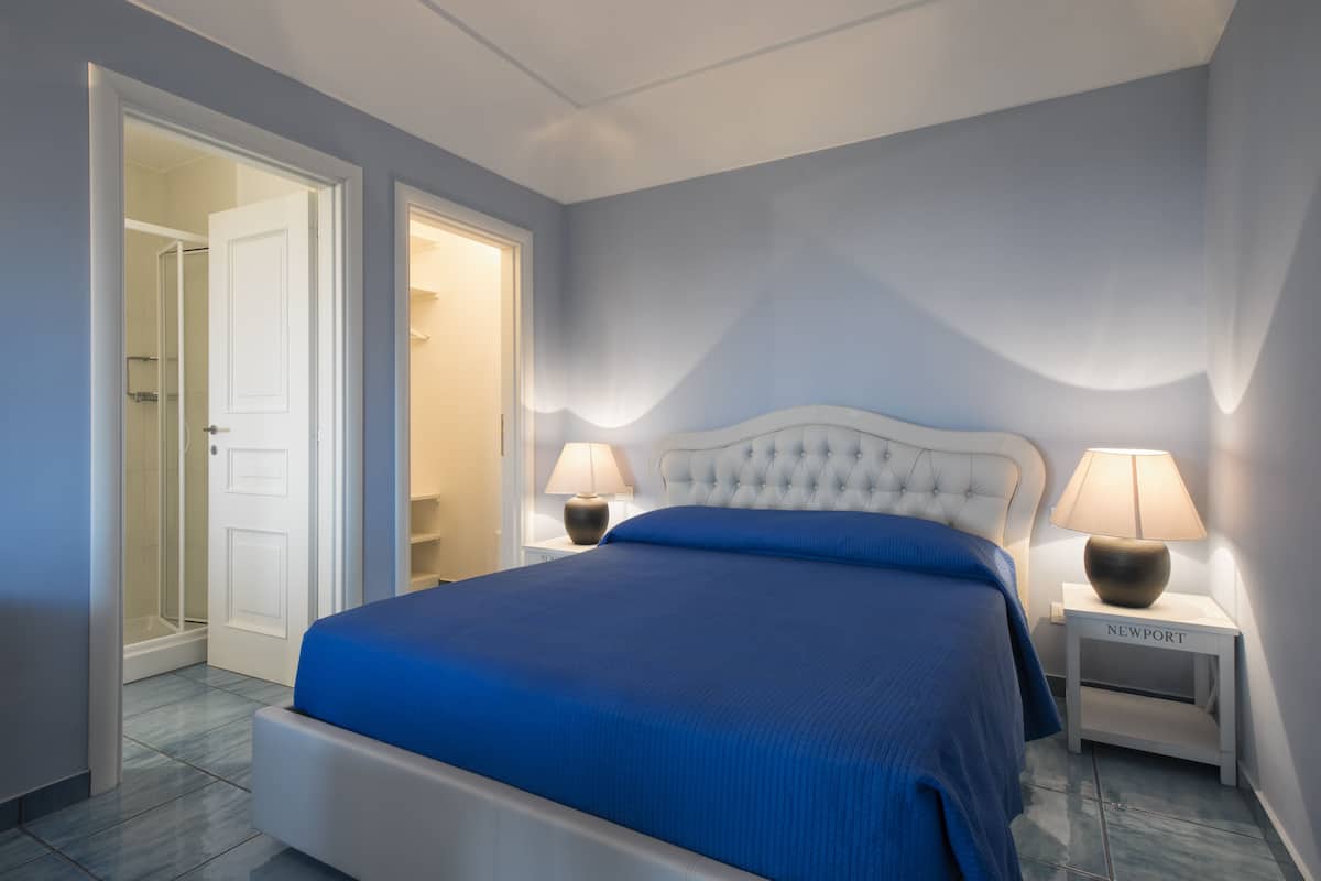 A bedroom with a bed, two bedside tables, a nightstand, and a door leading to a bathroom.
