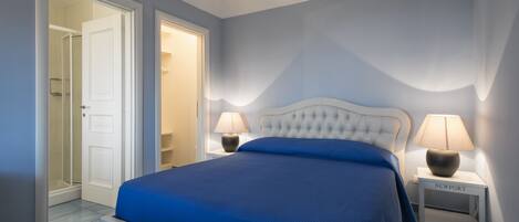 Un dormitorio con una cama, dos mesitas de noche y una puerta que da al baño.