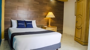 A hotel room with a large bed, a nightstand with a lamp, and a wooden wardrobe. - Capital O Hotel Dos Mares, Cabo San Lucas (Cabo San Lucas)