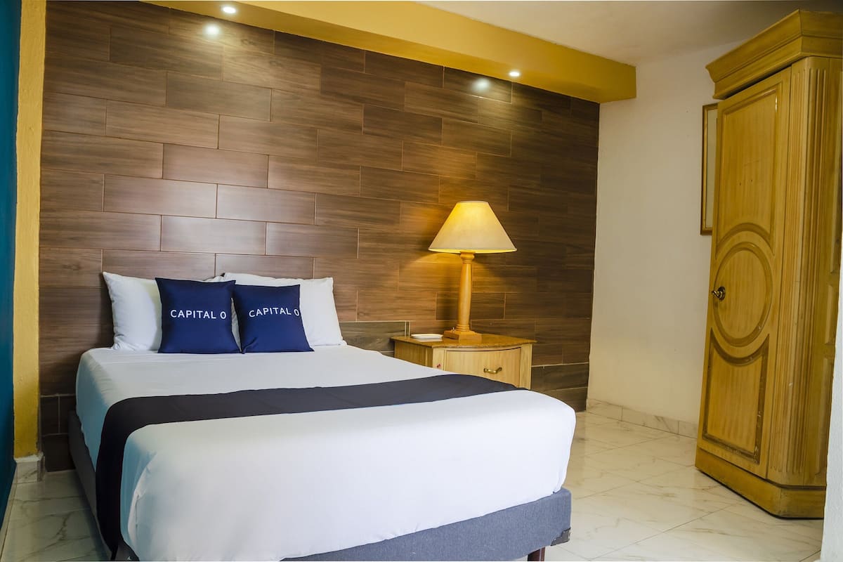 A hotel room with a large bed, a nightstand with a lamp, and a wooden wardrobe.
