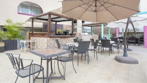 An outdoor patio area with a bar, dining tables, and chairs. - Capital O Hotel Dos Mares, Cabo San Lucas (Cabo San Lucas)