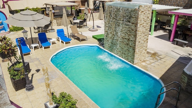 A swimming pool with lounge chairs and umbrellas, surrounded by a patio area with outdoor seating and a waterfall feature. - Capital O Hotel Dos Mares, Cabo San Lucas (Cabo San Lucas)