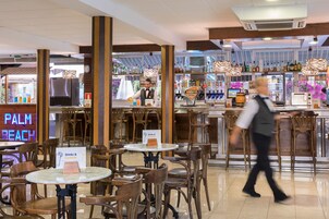 A bar area with wooden chairs and tables, a neon sign reading "PALM BEACH", and a bartender.