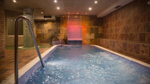 Un jacuzzi con escalera metálica, rodeado de muros de piedra y suelo de baldosas.