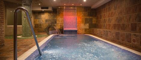 A hot tub with a metal ladder, surrounded by stone walls and a tiled floor.
