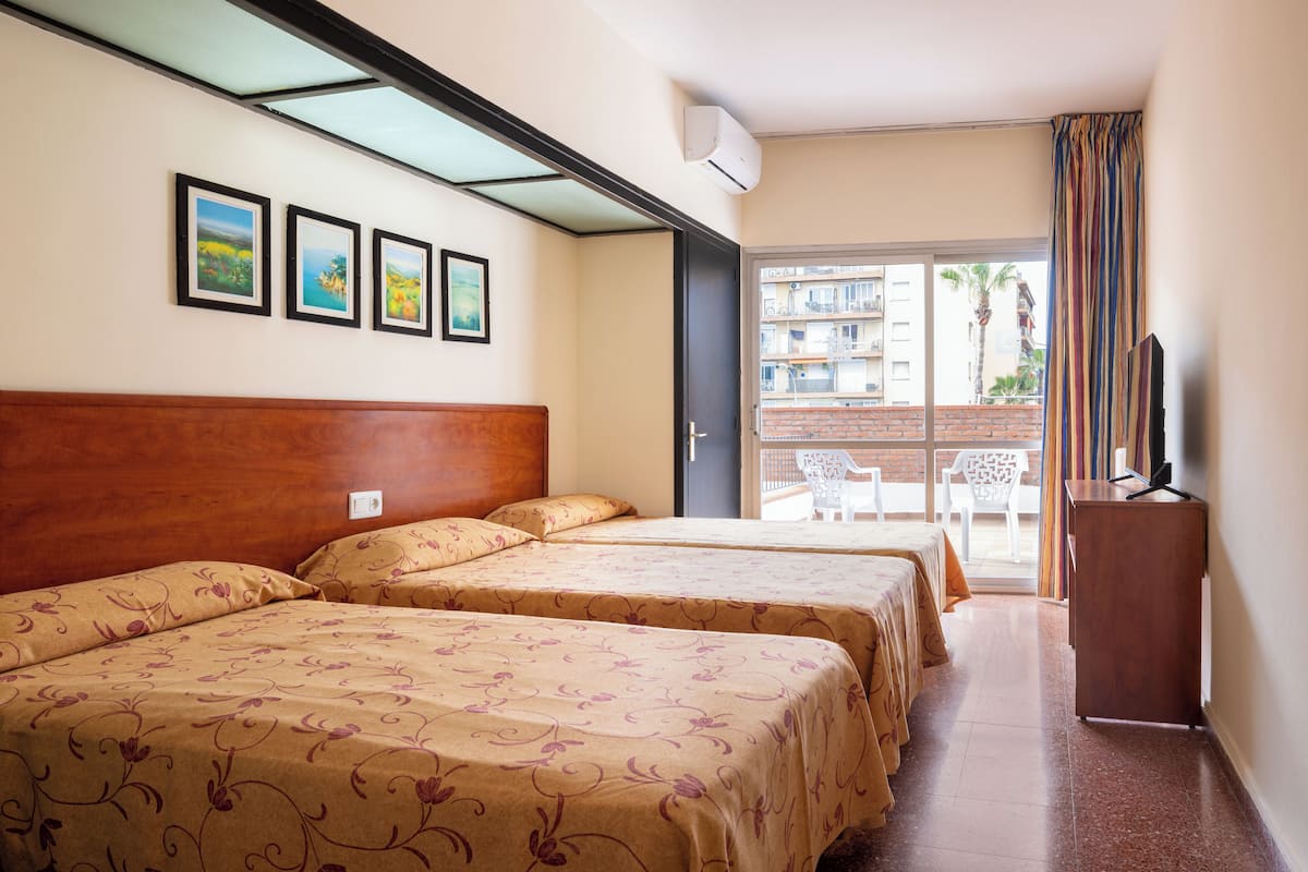 Une chambre d’hôtel avec deux lits, une tête de lit en bois, un balcon offrant une vue sur la ville et un téléviseur posé sur une commode en bois.