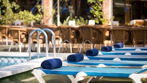 Un área junto a la piscina con sillones de descanso y sombrillas, un muro de ladrillo y una piscina.