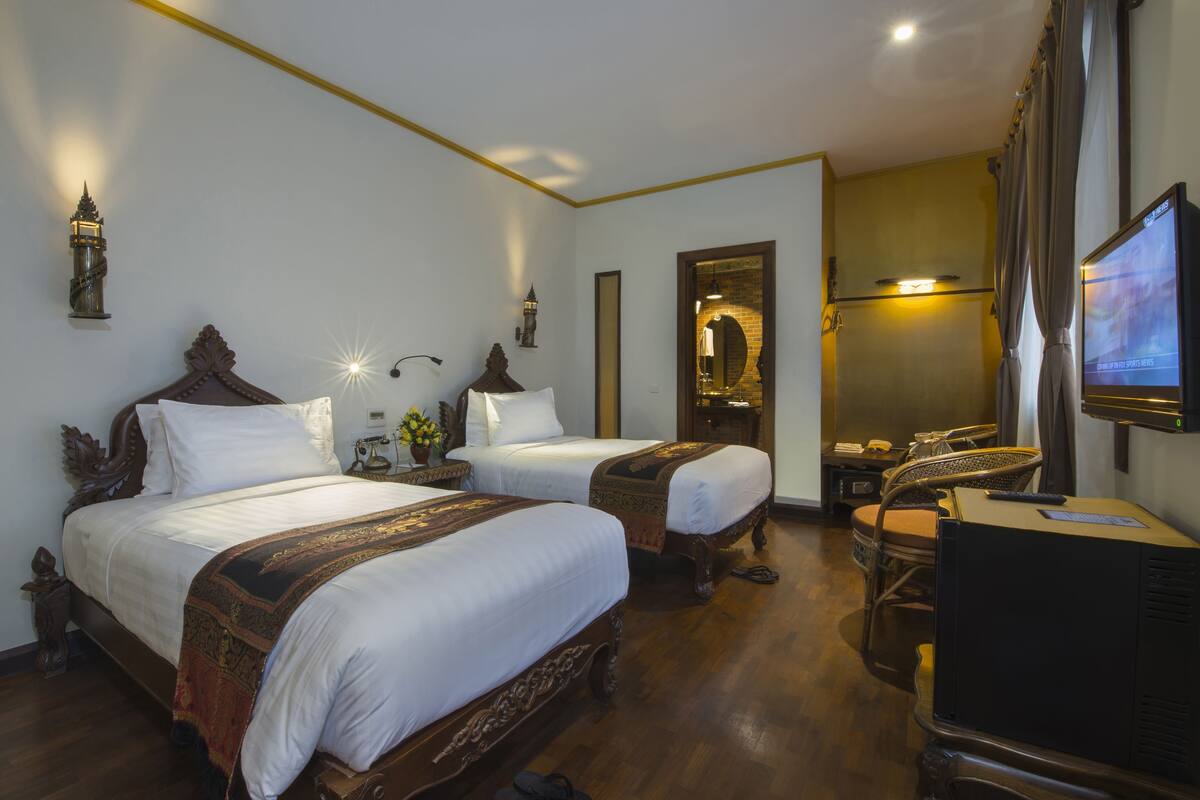 Habitación de hotel con dos camas, televisión, escritorio y espejo.